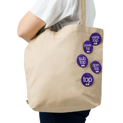 Gay top fetish pin badges clipped to a bag - LetGoGetLaid kink role badges for cruising and fetish events